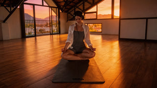 Young Woman meditating in a yoga studio at sunset in a tropical island on a yoga mat listenig to music with headphones