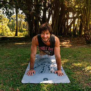 Man on a urca mat in a park with tropical trees in the background