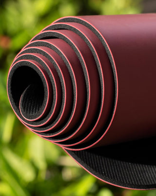 Roll of red and black yoga mat URCA with a blurred green background
