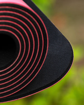 Close-up of a black and red yoga mat with a blurred green background